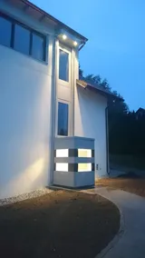 QuattroPorte-Außenaufzug am Wohnhaus in der Dämmerung mit beleuchteten Lichtbändern