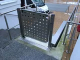 Obere Haltestelle des Rollstuhllifts an einer Außentreppe, Edelstahl-Tür mit Lochblech