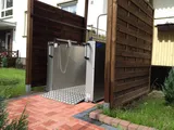 Rollstuhllift zwischen Holz-Sichtschutzwänden am Hauseingang, Plattform mit Auffahrrampe